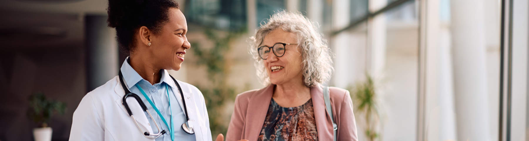 A female doctor with a stethoscope talking and smiling with an older female patient.