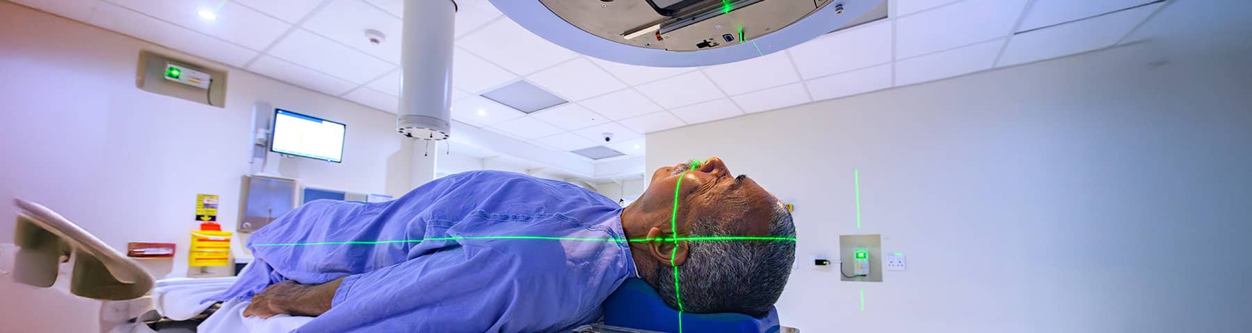 Patient receiving radiation therapy with laser alignment beams in a cancer treatment room.