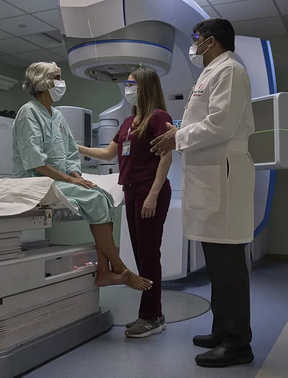 Patient speaking with medical staff in a radiation oncology treatment room.