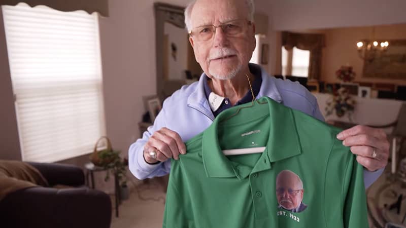Leonard Nussbaum holding his personalized green golf shirt.